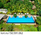 Aerial view of swimming pool, sunbeds and umbrellas, green palms, sandy beach in luxury resort at sunrise in summer. Nungwi, Zanzibar island. Top drone view. Tropical landscape. Exotic. Seaside. Стоковое фото, агентство Ingram Publishing / Фотобанк Лори
