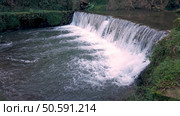 A powerful flow of water cascades over a man-made weir near Cascata do Outeiro. The scene showcases the dynamic interplay of nature and human influence in Oliveira de Azemeis. Стоковое фото, агентство Ingram Publishing / Фотобанк Лори