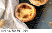 A close-up of a Portuguese custard tart with a slightly burnt top, resting on a black cooling rack next to a folded white cloth. Стоковое фото, агентство Ingram Publishing / Фотобанк Лори