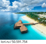 Aerial view of bungalow, white sandy beach, ocean on summer sunny day. Restaurant on the sea. Top drone view of wooden hotel, azure water, palms, sky with clouds. Luxury resort in Kendwa, Zanzibar. Стоковое фото, агентство Ingram Publishing / Фотобанк Лори