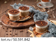 Tiramisu chia puddings elegantly served in glass cups, topped with cocoa powder and coffee beans, styled with a rustic wooden table and soft fabric. Стоковое фото, агентство Ingram Publishing / Фотобанк Лори