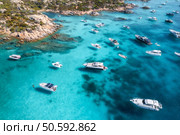 Aerial view of luxury yachts and boats navigating clear turquoise waters of the mediterranean sea near a rocky coastline with sparse vegetation. Top drone view. Summer vacation in Sardinia, Italy. Aerial view of luxury yachts and boats enjoying the crystal-clear turquoise waters of a stunning cove in sardinia, italy, creating a picturesque scene of summer leisure and idyllic escape. Стоковое фото, агентство Ingram Publishing / Фотобанк Лори