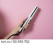 White curling iron in a woman’s hand on a pnk background. An accessory for creating hairstyles. Beauty and fashion. Hair care. Стоковое фото, агентство Ingram Publishing / Фотобанк Лори