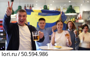 Company of excited young adult sports fans waving flag of Sweden and supporting national team with beer in bar. Стоковое видео, видеограф Яков Филимонов / Фотобанк Лори