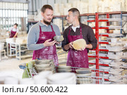 Friendly artisans examining and conferring over slipcast ceramic dishes in workshop. Стоковое фото, фотограф Яков Филимонов / Фотобанк Лори