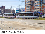 Two modern trams stand on the tracks in an urban setting, reflecting the cityscape in their windows. Russia, Krasnodar. Редакционное фото, фотограф Коханова Наталья / Фотобанк Лори
