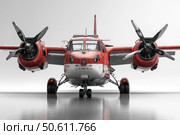 Frontal view of a twin-engine propeller aircraft with bright red paint and white elements on the fuselage. The aircraft is on a wet runway with reflection on the shiny surface. Details of the engines, propellers, chassis and cockpit are visible. The shooting was done in a studio with a flat white background, emphasizing the technical and design features of the aircraft. The image is perfect for aviation, transport, engineering and military equipment themes. Стоковое AI-изображение, AI-художник Анна Кривицкая / Фотобанк Лори