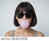 Молодая женщина в черных очках надувает пузырь из жвачки / A woman with short dark hair and black glasses inflates a pink bubble from a piece of gum. Стоковое AI-изображение, AI-художник Валерий Лукин / Фотобанк Лори