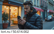 Hispanic young attractive man stands in dark street in front of shop, changes songs and tracks on smartphone, listens to music in wireless headphones. Hipster wearing casual dress. Стоковое AI-видео, аниматор Sergey Grishin / Фотобанк Лори