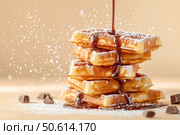 A stack of golden-brown Belgian waffles draped in glossy chocolate syrup. The powdered sugar dusts the edges, adding elegance to this visually appealing breakfast treat. Стоковое AI-изображение, AI-художник Nart / Фотобанк Лори