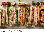 Delicious submarine sandwiches with fresh vegetables, meat and cheese filling a table. Стоковое AI-изображение, AI-художник Иван Рябоконь / Фотобанк Лори