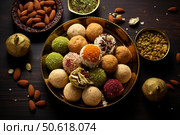 Delicious diwali sweets laddu or laddoo decorated with pistachios and almonds on a wooden table. Стоковое AI-изображение, AI-художник Иван Рябоконь / Фотобанк Лори