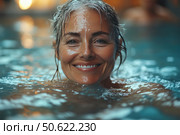 Portrait of a smiling elderly woman enjoying a swim in a pool with warm water. Her face is wet from the water, and her expression is bright, cheerful and peaceful. In the background there is a soft bokeh and warm lighting, creating an atmosphere of relaxation and comfort. The image conveys moments of happiness, self-care, an active and harmonious lifestyle in adulthood. Suitable for themes of health, spa, longevity, confidence and joy of life. Стоковое AI-изображение, AI-художник Анна Кривицкая / Фотобанк Лори
