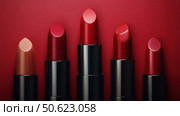 A collection of passion red lipsticks displayed against a vibrant red background. Beauty industry concept. Copy space. Advertisement for makeup artists. Стоковое AI-изображение, AI-художник Ирина Михайличенко / Фотобанк Лори