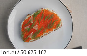 Delicious toast with cream cheese, red caviar and lemon slices, a traditional Eastern European appetizer, is presented on a white plate with black cutlery. Стоковое видео, видеограф Данил Руденко / Фотобанк Лори