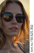 Woman with blonde hair wearing sunglasses at the beach during sunset. Relaxed summer evening and coastal lifestyle concept. Стоковое AI-видео, аниматор Sergey Grishin / Фотобанк Лори