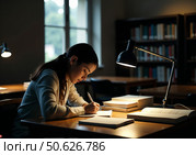 Студентка университета сидит за столом в библиотеке и пишет в тетради. A university student is sitting at a table in the library, writing in a notebook. Стоковое AI-изображение, AI-художник Смирнова Светлана / Фотобанк Лори