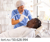 Aesthetician applying atomized nutrients onto black man face. Стоковое фото, фотограф Яков Филимонов / Фотобанк Лори