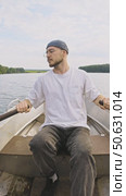 A young brutal man paddles while sailing on a metal rowboat on the lake. vertical. Стоковое видео, видеограф Strunov David / Фотобанк Лори