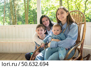 Мать с тремя детьми позируют для фотографии. Брат и сестра-подростки, младший брат и мать сидят в белой беседке летом на свежем воздухе. Стоковое фото, фотограф Яна Проничева / Фотобанк Лори