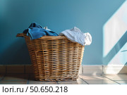 Wicker laundry basket overflowing with clothes in a sunlit bathroom. Стоковое AI-изображение, AI-художник Иван Рябоконь / Фотобанк Лори