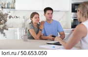 Smiling young couple discussing new home choice with female real estate agent showing options for residence on laptop while sitting at kitchen table. Стоковое видео, видеограф Яков Филимонов / Фотобанк Лори