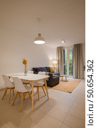 Wide shot of minimalist living and dining area with white dining table, gray sofa, floor lamp and large window. Стоковое фото, фотограф PAv / Фотобанк Лори