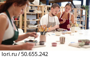 Female teacher and mentor helps students learn how to make patterns on ceramic plates using paint and brush in a pottery workshop. Стоковое видео, видеограф Яков Филимонов / Фотобанк Лори