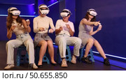 Four cheerful emotional young female friends in VR goggles sitting in virtual reality room, manipulating objects or shooting at targets with gaming controllers in hands. Стоковое видео, видеограф Яков Филимонов / Фотобанк Лори