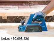 A hand-held electric planer in the hands of a craftsman. A man planing boards with an electric tool. Production of wooden products. Construction, wood processing. Стоковое фото, фотограф Photojuli / Фотобанк Лори