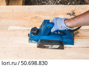 A hand-held electric planer in the hands of a craftsman. A man planing boards with an electric tool. Production of wooden products. Construction, wood processing. Стоковое фото, фотограф Photojuli / Фотобанк Лори