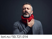 Mature man suffering from sore throat touching neck wearing scarf on dark background. Стоковое AI-изображение, AI-художник Иван Рябоконь / Фотобанк Лори