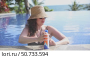 Young woman wearing straw hat applies sunscreen spray while relaxing in a pool during summer tropical vacation. Sun protection, leisure and enjoying sunny outdoor moments concept. Slow motion footage. Стоковое видео, видеограф Ирина Михайличенко / Фотобанк Лори
