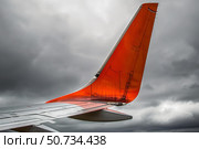 Orange airplane winglet flying through cloudy sky. Стоковое AI-изображение, AI-художник Иван Рябоконь / Фотобанк Лори