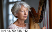 Senior professional harpist playing with elegant harp in concert hall. Стоковое AI-изображение, AI-художник Юрий Поздников / Фотобанк Лори