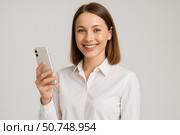 Smiling Woman in a White Shirt Holding a Smartphone, Exuding Confidence and Approachability in a Modern, Professional Setting. Стоковое AI-изображение, AI-художник Башкирова Анна / Фотобанк Лори