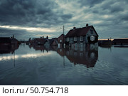 Flooded houses reflecting in water under dark cloudy sky. Стоковое AI-изображение, AI-художник Иван Рябоконь / Фотобанк Лори