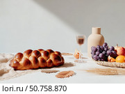 Rustic autumn table: challah bread, grapes, apples, and wine with natural decor. Стоковое AI-изображение, AI-художник Мария Фадеева / Фотобанк Лори