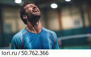 Exhausted male athlete in sportswear expressing frustration and fatigue after intense match, sweat glistening under indoor lights, capturing emotion and determination in competition. Стоковое AI-изображение, AI-художник Катерина Бондарец / Фотобанк Лори