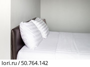 A neatly made bed with white linens and pillows stands against a gray wall in a minimalist hotel room. Стоковое фото, фотограф Коханова Наталья / Фотобанк Лори