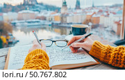 Cozy Winter Journaling with Cityscape View: Person Writing in Notebook, Warm Drink, Spectacles, and Stunning Urban Background. Стоковое AI-изображение, AI-художник Данила Большаков / Фотобанк Лори