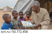 Teacher reading a book to african children in refugee camp. Стоковое AI-видео, аниматор Юрий Поздников / Фотобанк Лори