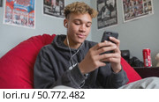 Teenager listening to music and texting on smartphone in bedroom. Стоковое AI-видео, аниматор Юрий Поздников / Фотобанк Лори