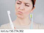 Happy woman compares a toothbrush with an electric one. The girl chooses oral hygiene products. Стоковое фото, фотограф Михаил Решетников / Фотобанк Лори