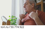 Senior Man shaving his face. Old male shaves beard and mustache with shaver. Elderly gray haired man looking at the mirror, applies shaving cream foam and using razor. Skin hygiene. Daily body care. Стоковое видео, видеограф Марина Демидюк / Фотобанк Лори