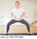 Pregnant woman is engaged in yoga. A pregnant woman practices yoga in the hall. Goddess Pose or utkata konasana. Стоковое фото, фотограф Татьяна Яцевич / Фотобанк Лори