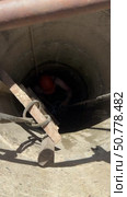 Man in construction helmet at the bottom of a mine shaft well. Assistant pulls up a bucket of sand with a rope. Cleaning of the mine shaft well. Vertical video. Стоковое видео, видеограф Vadzim Yakubovich / Фотобанк Лори