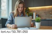A Young Woman is Engaged With Her Laptop at a Tidy Kitchen Table, Smiling Happily While Looking at the Camera. Стоковое AI-видео, аниматор Sergey Grishin / Фотобанк Лори