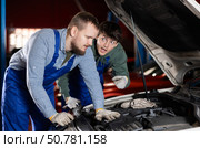 Two auto mechanics work together to diagnose an engine under the hood of a car in repair shop. Стоковое фото, фотограф Яков Филимонов / Фотобанк Лори
