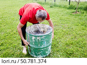 Pulling plastic liner tightly inside rain barrel, gardener ensures liner fits snugly along inner surface of watering barrel in backyard garden. Стоковое фото, фотограф Владимир Григорьев / Фотобанк Лори